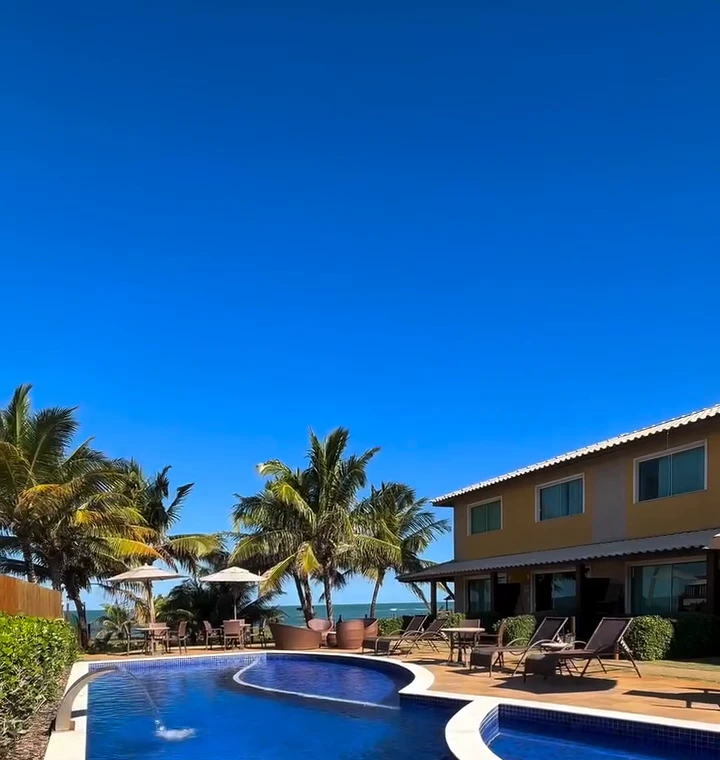 Piscina com cascata e fachada frente ao mar do condomínio na Praia do Portinho